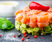 Délicieuse salade d'avocat et de saumon cru, tartare, servie sur une plaque noire au citron vert, fond clair