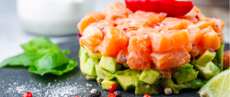 Délicieuse salade d'avocat et de saumon cru, tartare, servie sur une plaque noire au citron vert, fond clair
