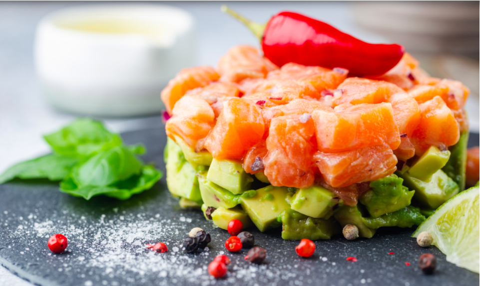 Délicieuse salade d'avocat et de saumon cru, tartare, servie sur une plaque noire au citron vert, fond clair