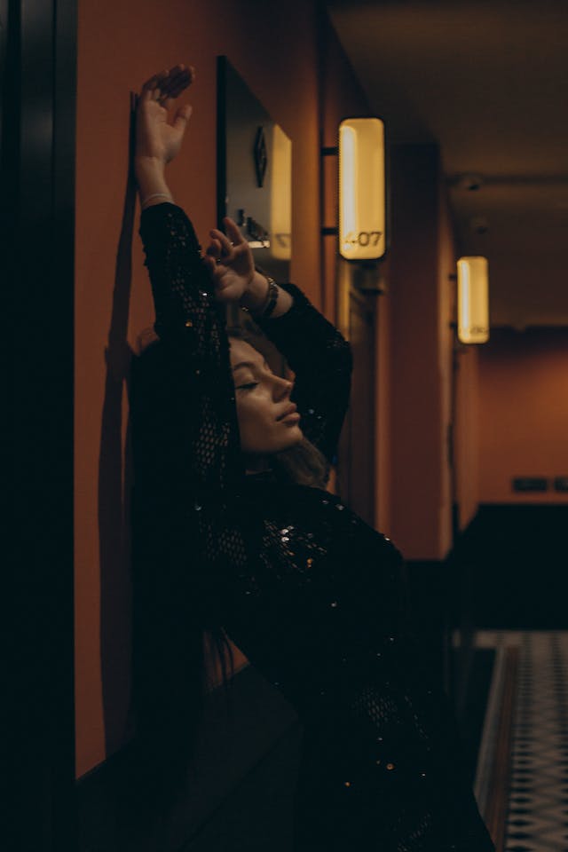 Une femme adossé à un mur de couloir, bras en l'air, semble prendre du plaisir.