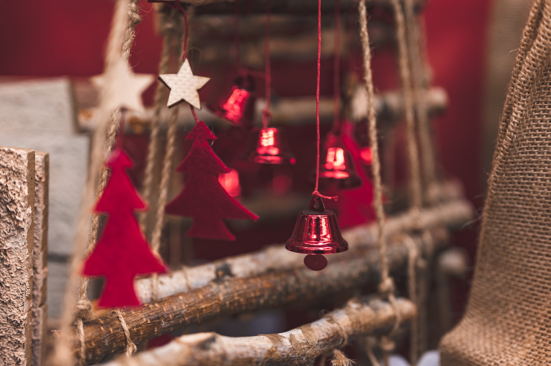 Décors de Noël, petits sapins de carton rouge et clochettes brillantes rouges sur fond de branchettes de bois et de toile de jute.
